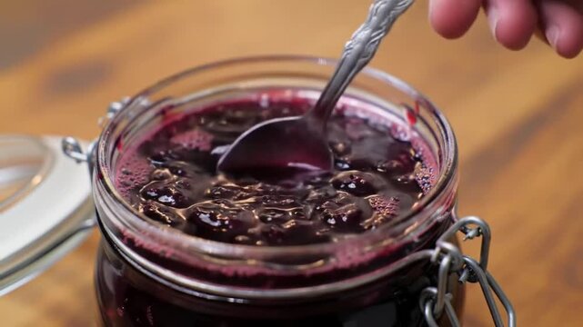 Hand stirring homemade berry jam with oats in a glass jar, close-up view