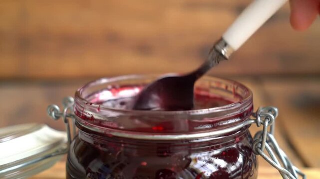 Scooping sweet homemade berry jam from a glass jar with a spoon