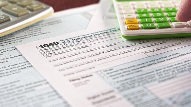 Taxpayer's hand using a calculator to fill out the united states individual income tax return form 1040 for tax season