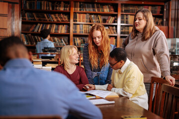 Students study together in a library, sharing notes and discussing a book in a quiet study group