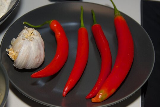 Fresh Red Chili Peppers and Whole Garlic Bulb on Dark Plate