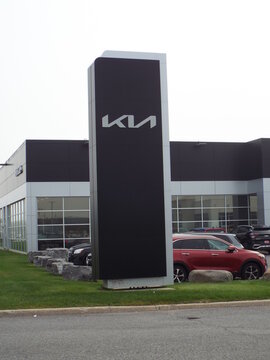 Nepean, ON, Canada-July 13,2025: A tall black "Kia pylon sign" stands in front of a modern grey dealership building on W Hunt Club Rd.
