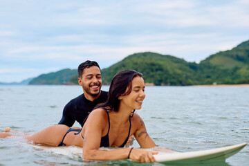 Obraz premium Young couple on a surfboard, smiling and learning to surf. Enjoying a fun summer activity on a beautiful day