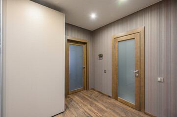 A modern hallway with frosted glass doors, striped grey wallpaper, wooden flooring, built-in wardrobe, recessed ceiling light, and minimalist wall fixtures