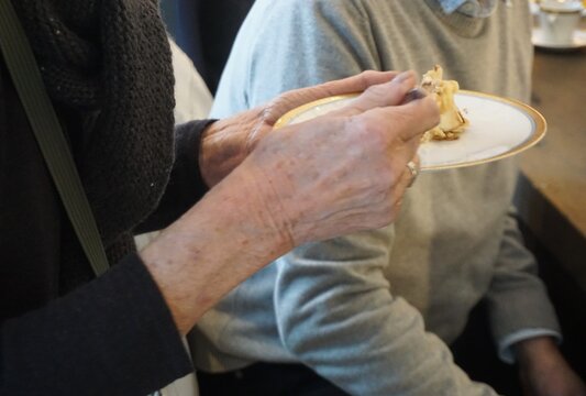 Oberk&ouml;rper von alter schlanker Frau mit schwarzem Wollpullover mit Muster beim Kuchen essen auf Fest in Raum