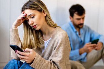Young couple sitting back to back, both focused on their smartphones, appearing emotionally distant