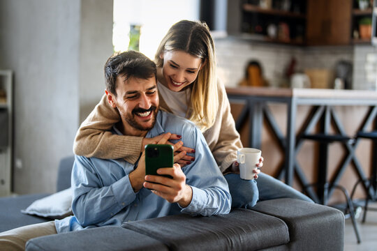 Smiling couple embracing while looking at smartphone. People sharing social media on cellphone.