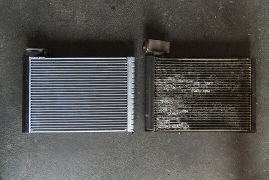 Top view comparison between a new clean aluminium car air conditioner evaporator and an old clogged cooling coil on a dark floor. Auto maintenance concept.