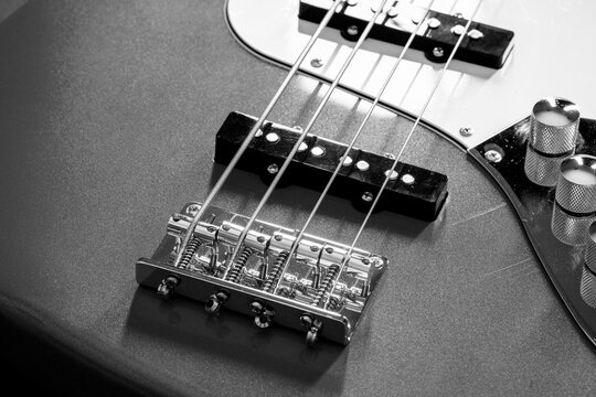 Close-up detail of a red four-string electric bass guitar showing strings, bridge and pickups. Music instrument background.

