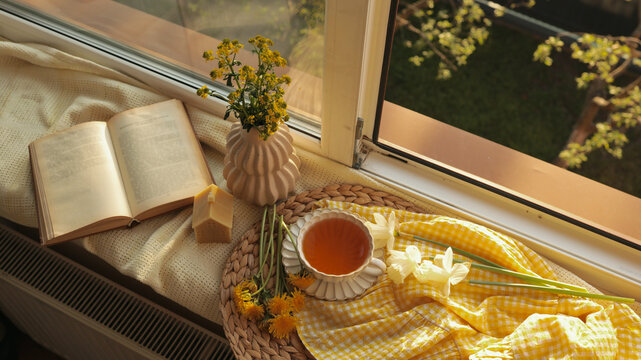 Cozy morning scene with open book, tea, and flowers by the window