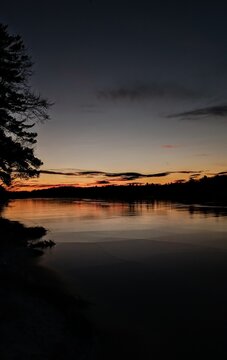 Moody blue hour sunset over Long Pond in Somerville Maine, dark silhouette forest and lake reflection, New England nightfall concept
