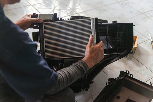 Close-up of a mechanic's hands assembling a new aluminum cooling coil into the car A/C housing unit during maintenance repair.