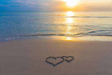 Two hearts drawn in the sand on the beach at sunset