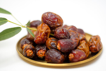 Sweet Dried Dates Piled on a Small Golden Plate with a Green Leaf Garnish Against White Background
