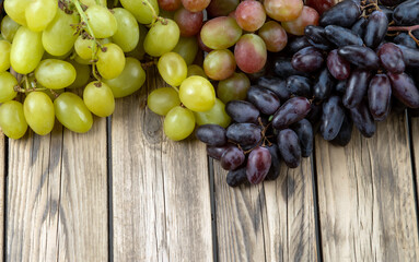 Assorted grape varieties in black, red, and green on a background of a wooden texture.