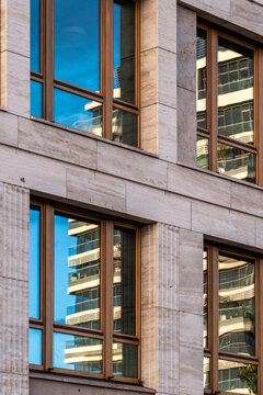 Urban building architecture with modern stone facade where corporate office windows catch reflection and create structured city pattern