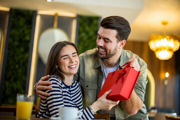 Fototapeta premium Man surprising a woman with a gift while sitting in a restaurant