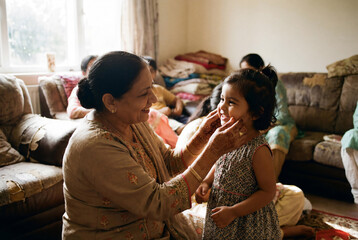 Obraz premium Happy Smiling Grandmother With Henna Tattoo Touching Cheeks Of Little Granddaughter During Eid Al Fitr Celebration At Home