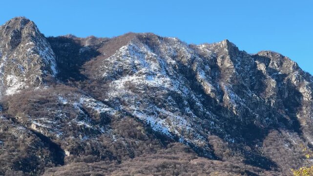 panning shot of snow covered mountains with peaks against a clear blue sky
