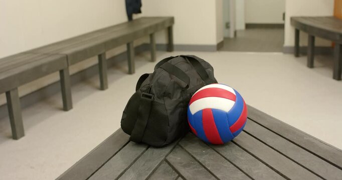 On recording start, black duffel bag and volleyball sitting on locker room bench awaiting practice