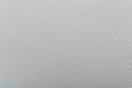 Water droplets on glass with a grey background create a textured surface during rainy weather in the afternoon light