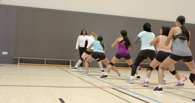 African American coach signaling diverse female team shuffling low in gym for defense, copy space