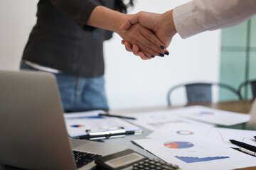 Businesspeople shaking hands in the meeting over a desk with business documents and laptop for the...
