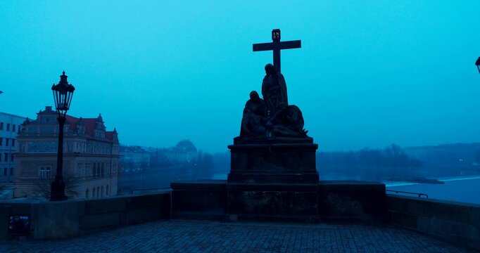 Dark winter morning details of historic statues on Charles Bridge in Prague. Moody blue tones and cold atmosphere create a dramatic and mysterious European city scene.