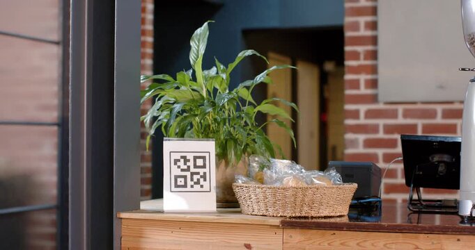 Camera is pushing and panning, centering cafe counter display, showing plant, QR sign, pastries