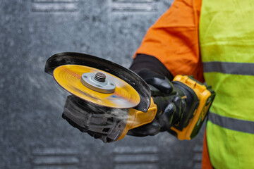 Close-up of a worker using a yellow angle grinder with spinning disc. Builder wearing safety gloves and vest. Concept of construction, metalworking, and industrial power tools in action.
