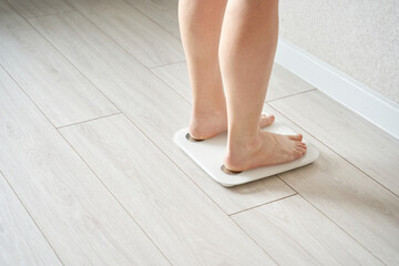 Caucasian female feet on scale: young adult monitoring weight on wooden floor for health and fitness goals.