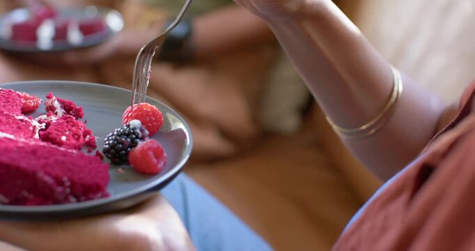 Woman is spearing raspberry on magenta cake plate on lap as fork is settling, to eat