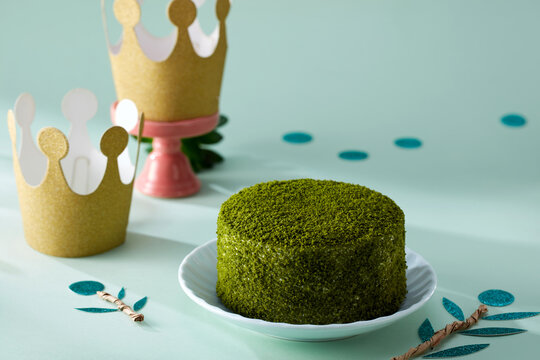A round matcha cheesecake on a pinkish-green table wtih decorate