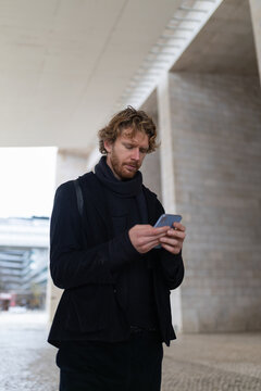 Young man using smartphone communicating online in urban setting