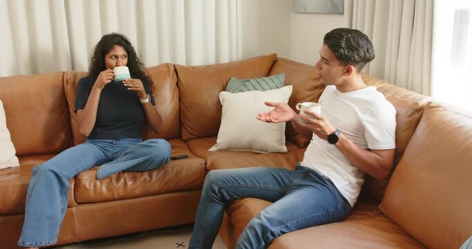 Couple sitting on brown sofa, man starting relaxed chat while woman lowering mugs and responding