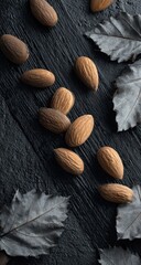 Close-up of almonds scattered on a dark, textured surface with grey leaves