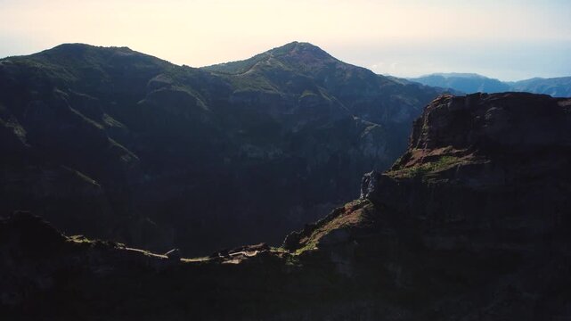 Aerial flyover of Pedra Rija ridge on PR1 trail in Madeira, drone flying forward over hikers on narrow mountain path towards massive cliffs near Pico do Areeiro, cinematic adventure landscape.