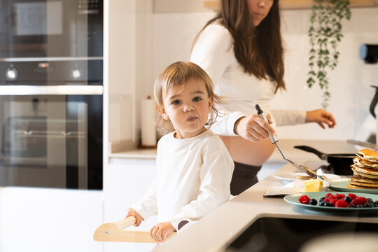 Child in kitchen with parent making breakfast during morning time
