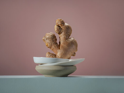 Ginger root on a stack of bowls against a soft pink background.