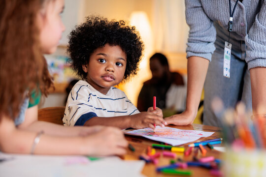 Children drawing with crayons, supervised by an adult.