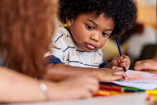 Child drawing with crayons, focused and creative.