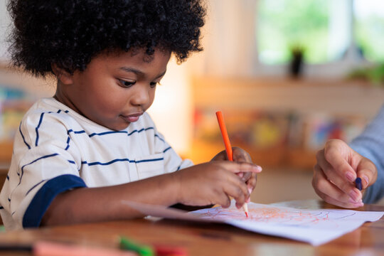 Child drawing with crayon, assisted by adult hand.