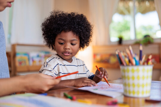 Child drawing with crayons, assisted by an adult.