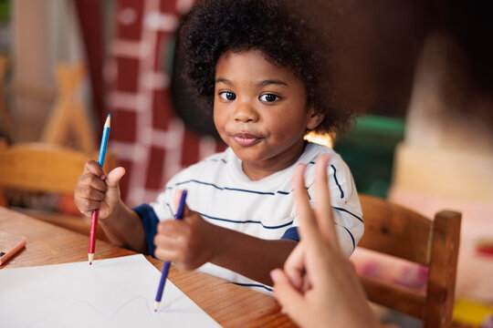 Child drawing with crayons at a table, getting help.