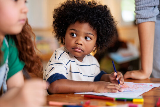 Child drawing with crayons, looking thoughtfully to the side.