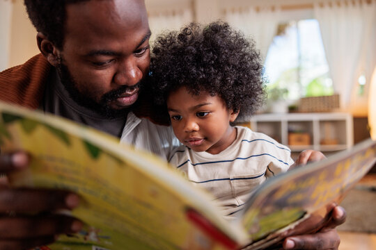 Father and son reading a book together indoors.