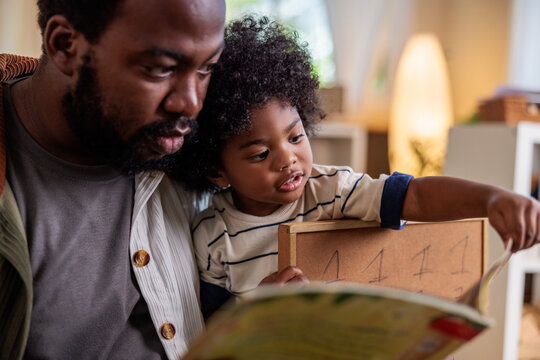Father and child reading a book together indoors.