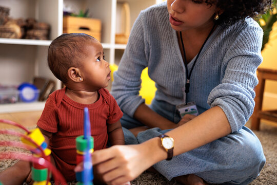 Baby looks up at caregiver playing with stacking toy.