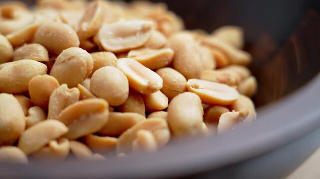 Close view of roasted salted peanuts in wooden bowl. Golden kernels with sea salt crystals