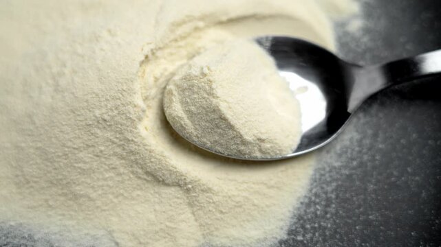 Metallic spoon filled with whey protein concentrate on black ceramic plate. Powdered sports nutrition component
